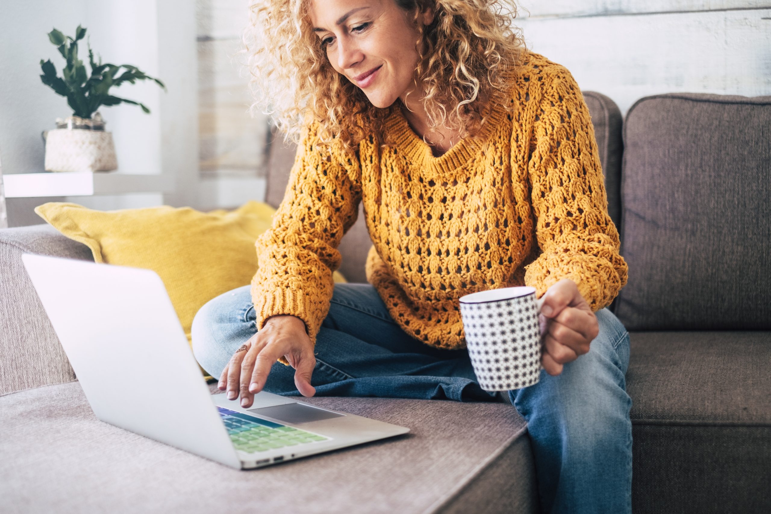 Nice beautiful lady with blonde curly hair work at the notebook sit down on the sofa at home - check on oline shops for cyber monday sales - technology woman concept for alternative office freelance